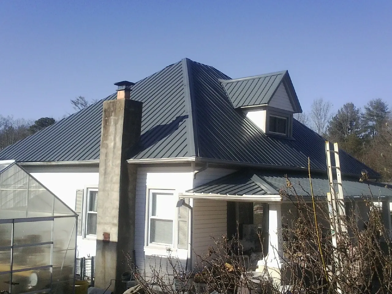 Dark blue standing seam metal roof on a white farmhouse with dormer — Slate & Tile Roof Repair by Roofing Brothers in Zebulon