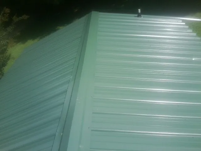 New green metal panels meeting at the ridge of a roof — Flat Roof Repair work by our crew in Zebulon