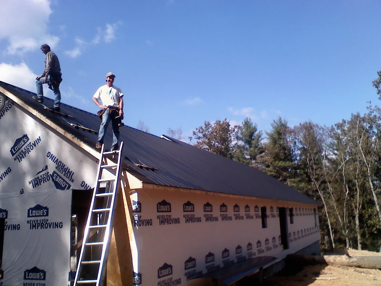 Two roofers standing on a long dark metal roof over a wrapped building in Zebulon
