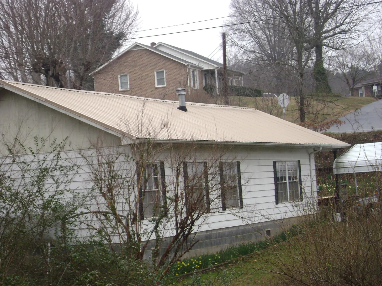 Tan metal roof on a white sided house set into a hillside — Commercial Roofing by Roofing Brothers in Zebulon