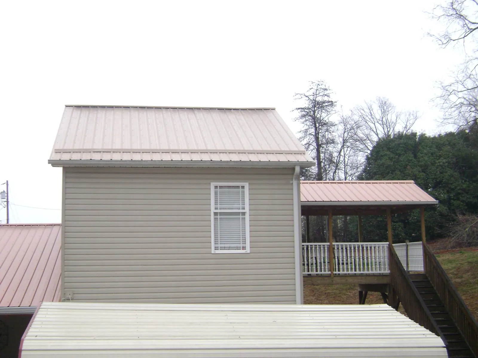 Tan metal roofs on a two story addition and attached porch, from a Roof Replacement job in Zebulon
